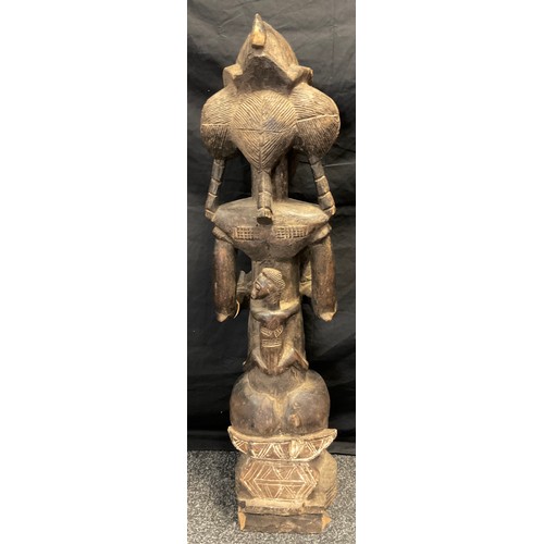 21 - An African Yoruba carved fertility figure, as a seated female, cradling a feeding baby, 93cm high