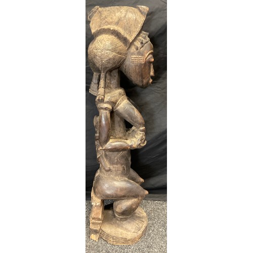 21 - An African Yoruba carved fertility figure, as a seated female, cradling a feeding baby, 93cm high