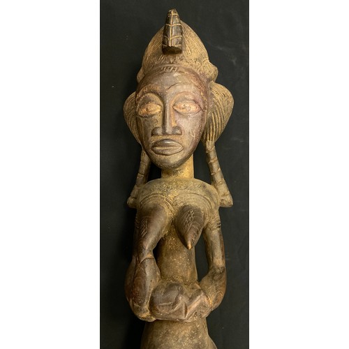 27 - An African Yoruba carved fertility figure, as a standing female, cradling a feeding baby, 97cm high