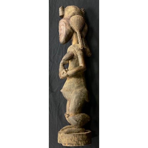 27 - An African Yoruba carved fertility figure, as a standing female, cradling a feeding baby, 97cm high