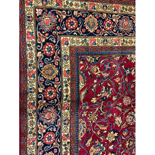 283 - A Persian Tabriz hand-knotted rug / carpet, the field in rich red with scrolling tendrils of stylise... 