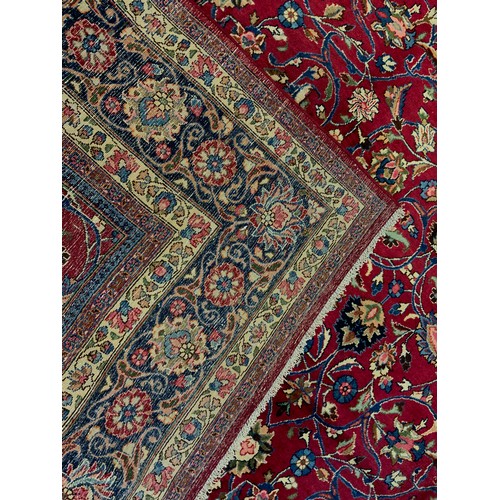 283 - A Persian Tabriz hand-knotted rug / carpet, the field in rich red with scrolling tendrils of stylise... 