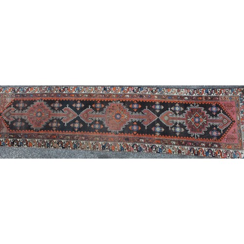 1018 - A Middle Eastern wool runner rug, rectangular field worked with hooked medallions, banded borders wi... 