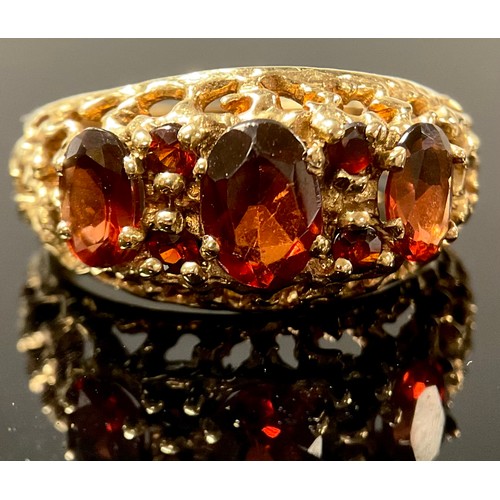 1184 - A 9ct gold and garnet three stone ring, the faceted oval cut stones graduating, fancy shank