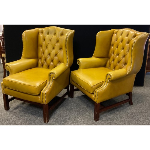 323 - A pair of George III style reproduction Chesterfield wing-back arm chairs, deep button backs, golden... 