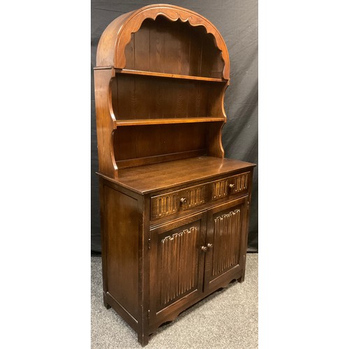 122 - An ‘Old Charm’ style oak arch-top dresser, plate-rack top, above a pair of short drawers, and two cu... 