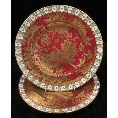 106 - A pair of Royal Crown Derby Gold Aves pattern shaped circular dinner plates, on a red ground, herald... 