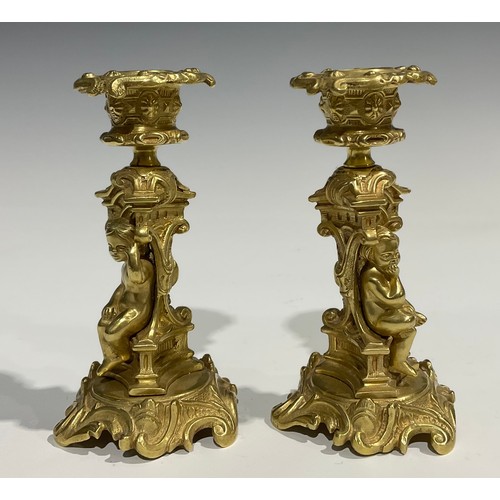 2082 - A pair of French Rococo style gilt bronze candlesticks, each stem with seated putti within sculpture... 