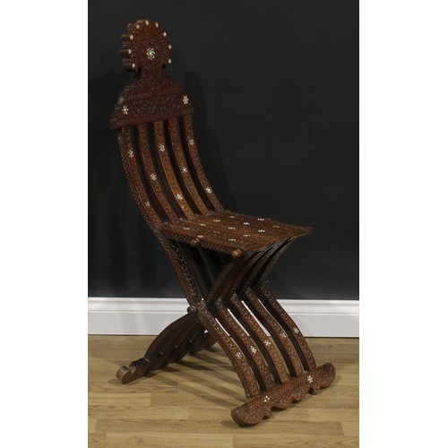 2573 - A Syrian hardwood and mother of pearl parquetry folding X-frame chair, profusely carved with scrolli... 