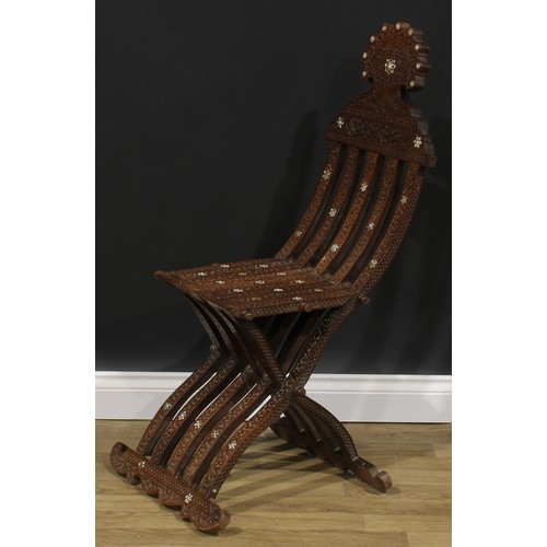 2573 - A Syrian hardwood and mother of pearl parquetry folding X-frame chair, profusely carved with scrolli... 