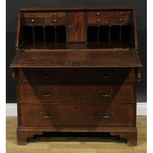 1940 - A George III oak bureau, fall front enclosing a small door, small drawers and pigeonholes, above fou... 