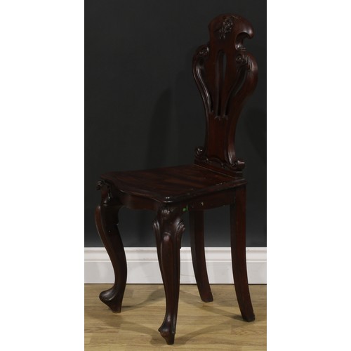 2535 - A pair of Victorian mahogany hall chairs, each with a pierced cartouche shaped back carved with a fl... 