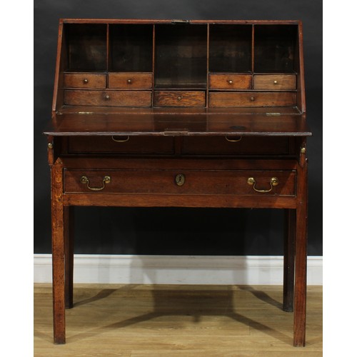 2041 - A George III vernacular oak bureau on stand, fall front enclosing small drawers and pigeonholes abov... 