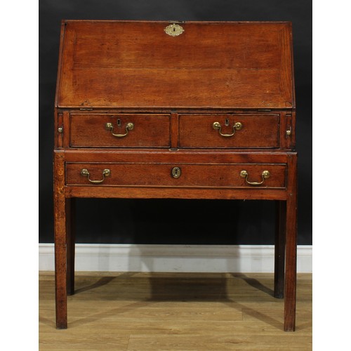 2041 - A George III vernacular oak bureau on stand, fall front enclosing small drawers and pigeonholes abov... 