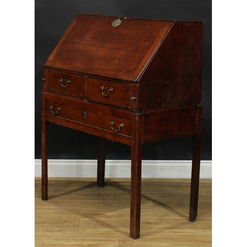 2041 - A George III vernacular oak bureau on stand, fall front enclosing small drawers and pigeonholes abov... 