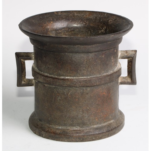 1679 - A cast iron pestle and mortar, flared rim above a quarter girdle, angular lug handles, skirted base,... 