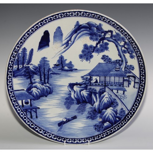 431 - A Japanese circular charger, painted in tones of underglaze blue with a pagoda in a monumental lands... 