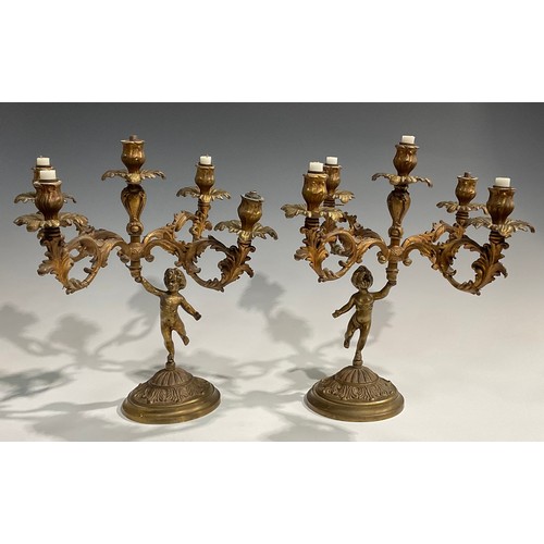 2093 - A pair of Rococo Revival gilt metal five light candelabra, each cast as a scantily clad putto holdin... 