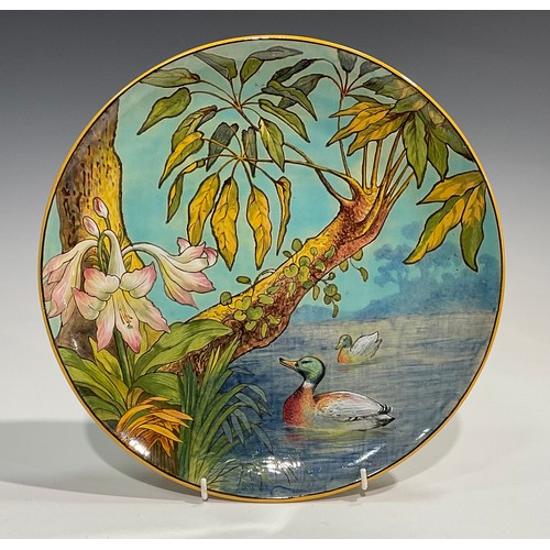 76 - An Aesthetic Movement circular charger, painted in polychrome with mallards at a riverbank, lilies a... 