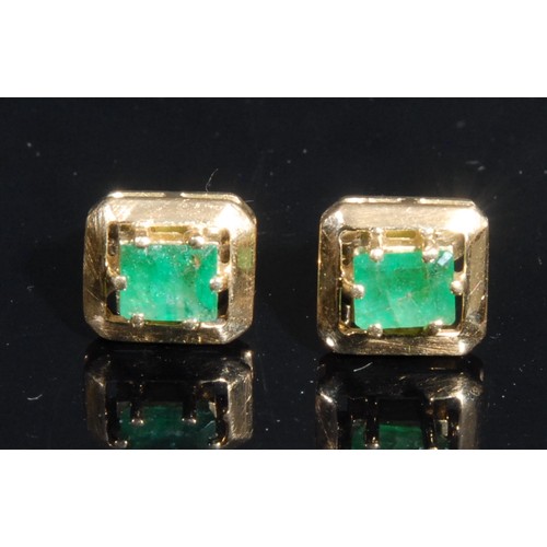 1433 - A pair of rectangular emerald solitaire ear studs, the cushion cut stone claw set within open work a... 