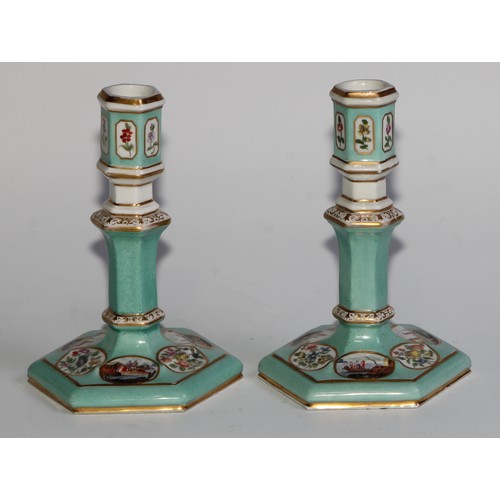 298 - A pair of Berlin hexagonal candlesticks, of silver shape, decorated in polychrome with landscape vig... 