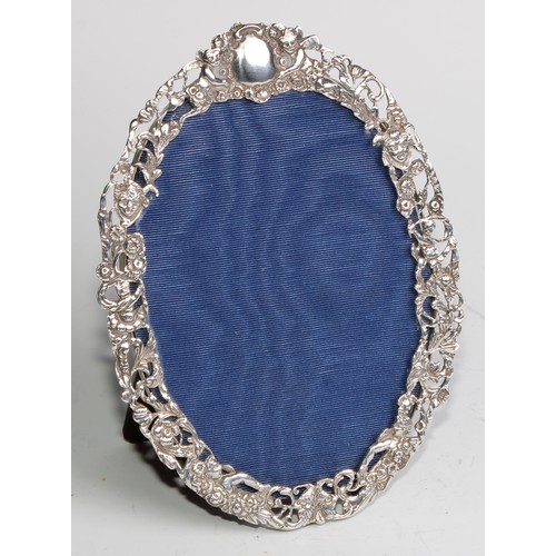 1174 - An Edwardian silver oval easel photograph frame, the pierced border cast with masks, flowers and lea... 