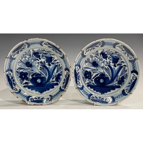 310 - A set of three Delftware chargers, boldly decorated in underglaze blue with flowers, 30.5cm diameter... 