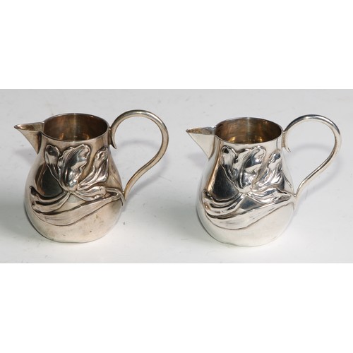 1030 - A pair of German Art Nouveau silver sparrow beak cream jugs, applied with stylised lilies in whiplas... 