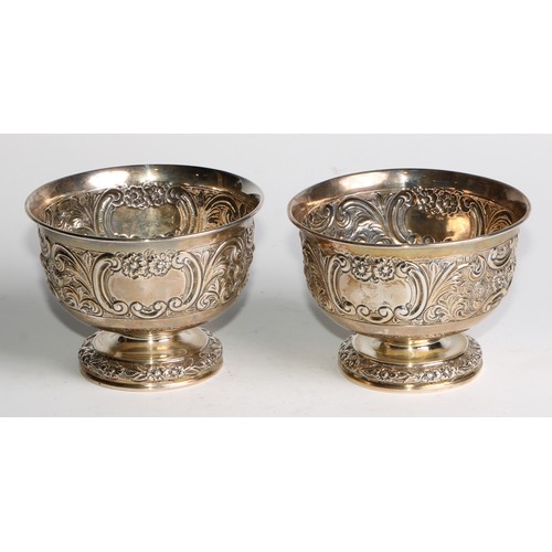 1037 - A pair of Victorian silver pedestal bowls, chased with flowers and scrolling leaves, centred by vaca... 