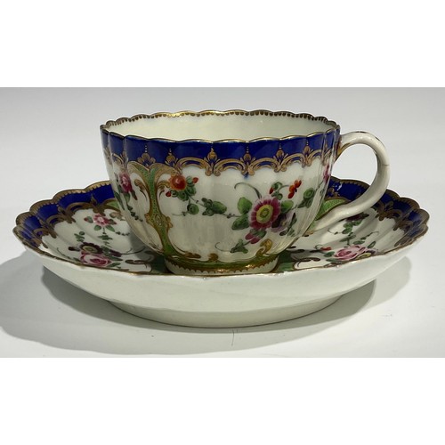 212 - A Worcester fluted teacup and saucer, painted with panels of colourful flowers on a green ground, bl... 