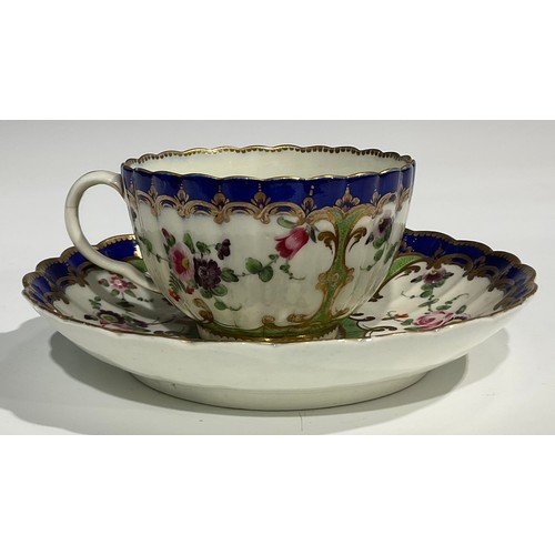 212 - A Worcester fluted teacup and saucer, painted with panels of colourful flowers on a green ground, bl... 