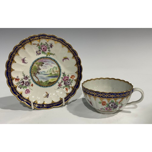 211 - A Worcester fluted teacup and saucer, circular cartouches painted with lakeside scenes, edged with a... 