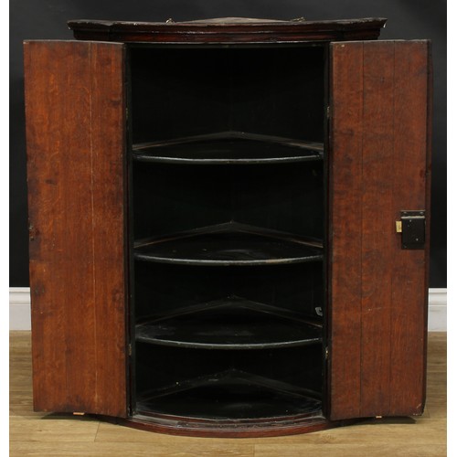 1939 - A George III oak bowfront corner cabinet, the pair of panel doors later carved in the Victorian era ... 