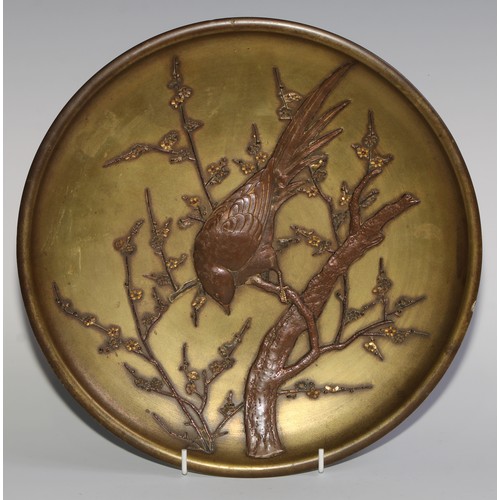 418 - A Japanese gilt and brown patinated bronze circular charger, applied with a bird on a blossoming pru... 