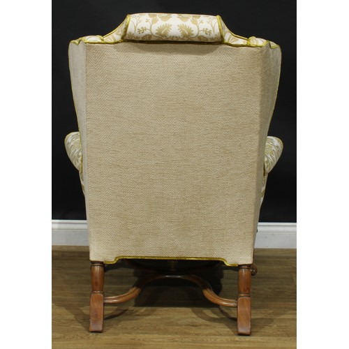 2180 - A William & Mary Revival wing chair, stuffed-over upholstery, squab cushion, shaped stretcher, Spani... 