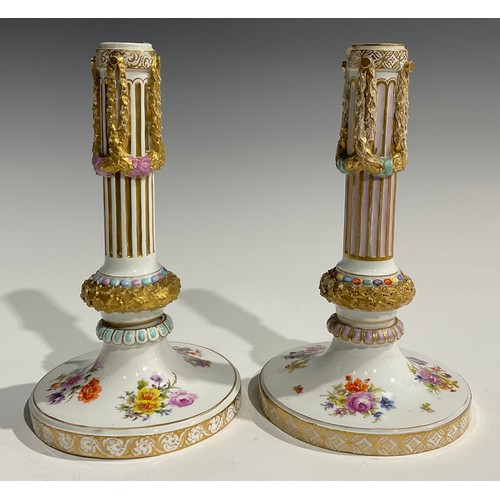 297 - A near pair of Continental porcelain candlesticks, the fluted columns moulded with swags, beaded and... 