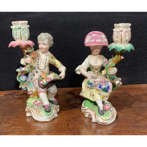 248 - A pair of Derby porcelain figural candlesticks, she seated with an apron of flowers, he holding his ... 