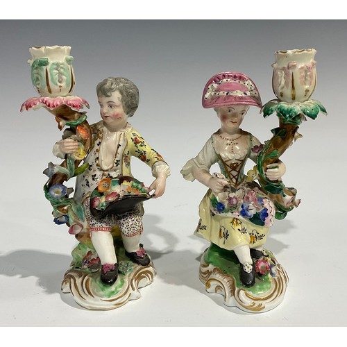 248 - A pair of Derby porcelain figural candlesticks, she seated with an apron of flowers, he holding his ... 