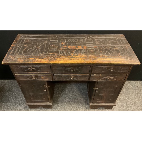 150 - A carved and stained pine knee-hole desk, carved to all sides with tribal inspired ‘panels’, six six... 