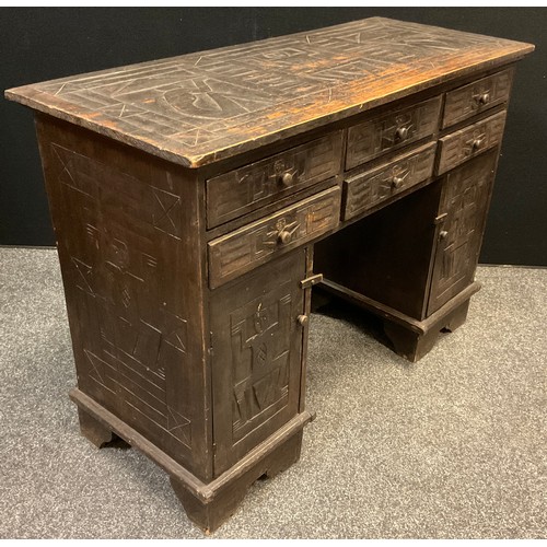 150 - A carved and stained pine knee-hole desk, carved to all sides with tribal inspired ‘panels’, six six... 