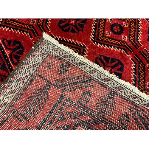 404 - A North Persian Meshed Belouch rug / carpet, hand-knotted in deep red and black, 250cm x 132cm.