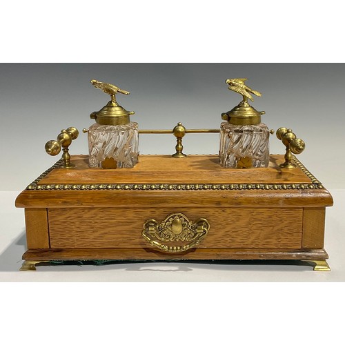 27 - A blonde oak desk standish, brass gallery, pair of clear glass inkwells, mounted with brass eagle fi... 