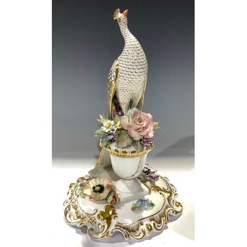 5 - A Royal Crown Derby Peacock, neck extended, seated upon a floral encrusted urn, quatrefoil base, pri... 