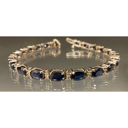 463 - A diamond and blue sapphire tennis bracelet, white metal mounts, stamped 14k, 17cm long, 13.3g gross