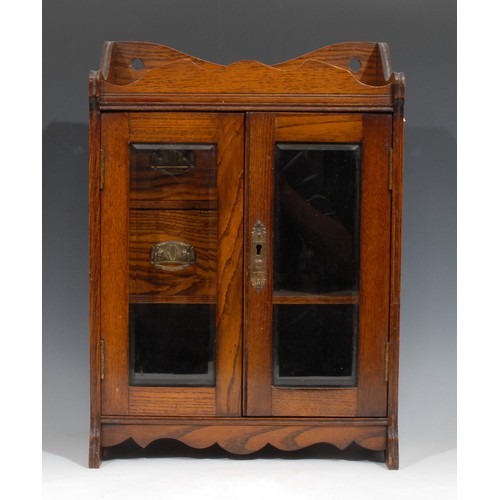 275 - A late Victorian oak smoking room cabinet, shaped cresting above a pair of bevelled glazed doors enc... 