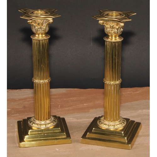 693 - A pair of brass Corinthian column candlesticks, detachable nozzles, fluted columns, stepped square b... 