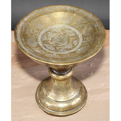 282 - A Middle Eastern brass pedestal stand, profusely chased and engraved in the Islamic taste with Arabi... 