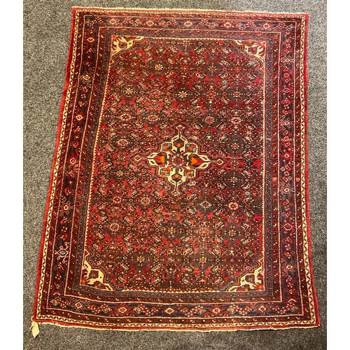 81 - A Middle Eastern woollen rug or carpet, geometric floral motifs, in tones of red, blue and ochre, 20... 