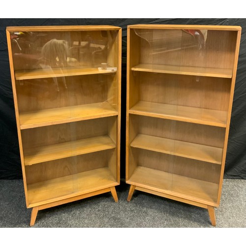 130 - A pair of mid century oak bookcase cabinets, each with three tiers of shelving, enclosed within pair... 