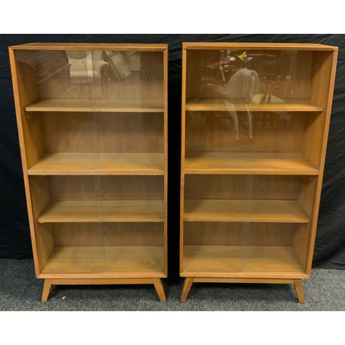 130 - A pair of mid century oak bookcase cabinets, each with three tiers of shelving, enclosed within pair... 